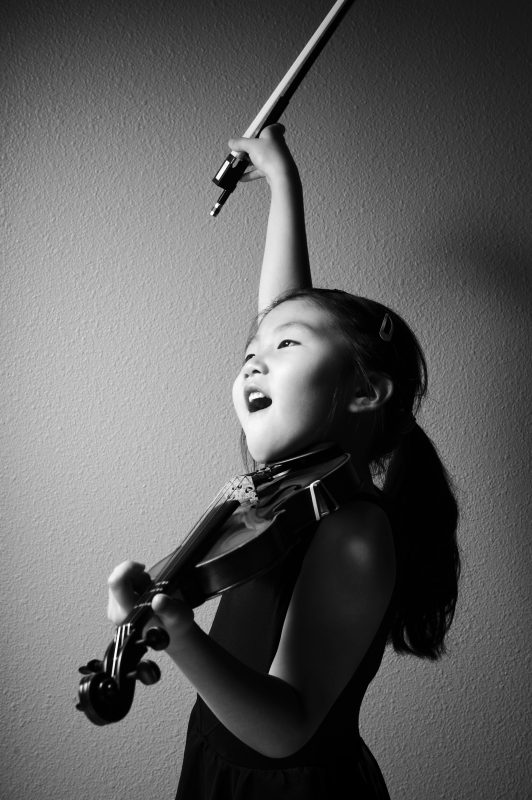 Little girl playing violin and lifting her arm up in joy. Representing violin lessons at SFE music school